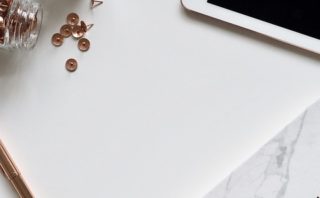 White desk top with rose gold thumb tags, white tablet, and a writing journal.