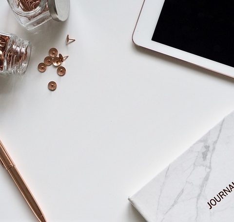 White desk top with rose gold thumb tags, white tablet, and a writing journal.